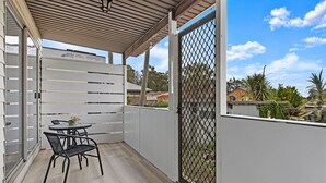 A covered balcony with a table and chairs, a metal gate, and a view of the neighborhood. - Kozyguru | Blacktown | Peaceful 3B House (Blacktown)