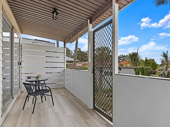 A covered balcony with a table and chairs, a metal gate, and a view of the neighborhood. - Kozyguru | Blacktown | Peaceful 3B House (Blacktown)