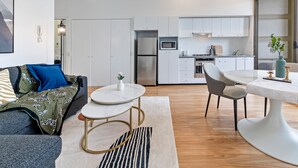 A modern living room with a sofa, coffee table, and dining area. It includes a kitchen with appliances and cabinets. - Kozyguru | Chippendale | Kozy Clean 1Bed Apt (Chippendale)