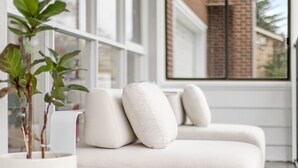 A modern living room with a white sofa, a potted plant, and a window with a view of a brick building. - Kozyguru | Forestville | Charming 3Br House (Forestville)