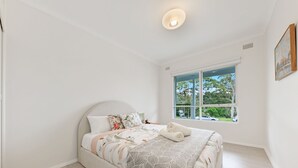 A bedroom with a bed, a window with a view of trees, and a ceiling light. - Kozyguru | Forestville | Charming 3Br House (Forestville)