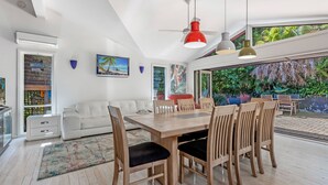 Un comedor moderno con una mesa y sillas de madera, un ventilador de techo rojo y vistas a un follaje exuberante.
