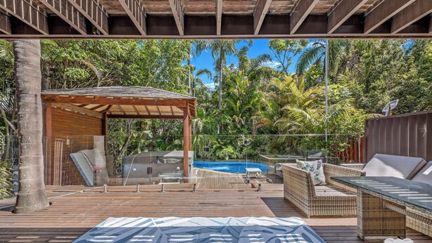 Terraza de madera con piscina, muebles de mimbre y un espacio de estar cubierto.
