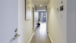 Un couloir étroit avec un plancher en bois, des murs blancs et une porte sur le côté gauche.