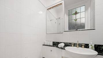 A bathroom with white tiles, a marble countertop, a sink, a mirror, and a window with a stained glass design.