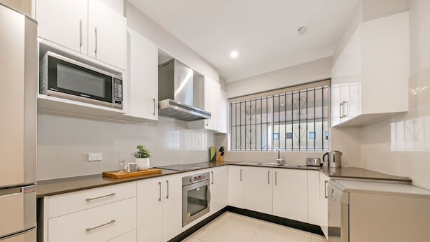 Een moderne keuken met witte kastjes, een magnetron, oven en een raam met decoratieve roede.