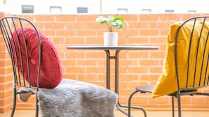Twee metalen stoelen met kussens, een tafeltje en een potplant op een balkon met een achtergrond van een bakstenen muur.