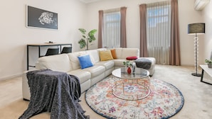 Een moderne woonkamer met een witte bank, een glazen salontafel en een kamerkleed met een patroon.