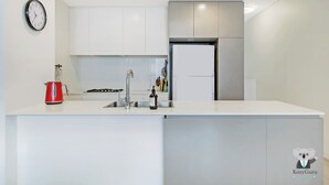 Une cuisine moderne avec des meubles blancs, un réfrigérateur en acier inoxydable, une bouilloire rouge et une horloge murale.
