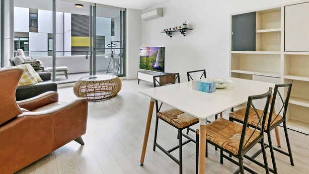 Un salon moderne avec un coin repas, comprenant une grande télévision, des meubles en osier et une porte vitrée donnant sur un balcon.