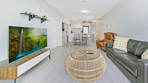 Un salon moderne doté d’un téléviseur à écran plat, d’une table basse ronde en osier, d’un canapé en cuir et d’un coin repas avec une table et des chaises blanches.
