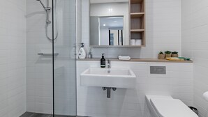 Un baño moderno con cabina de ducha de vidrio, un lavamanos blanco, un espejo y un inodoro.