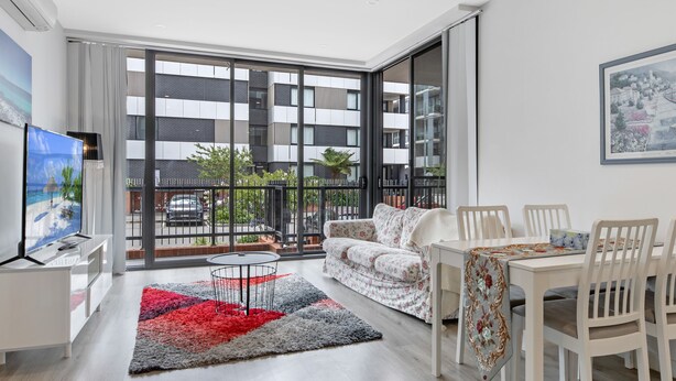 Una sala moderna con balcón, comedor y televisor sobre un mueble.