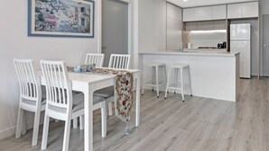 Una cocina moderna con armarios blancos, una isla central y un comedor con sillas y una mesa blancos.