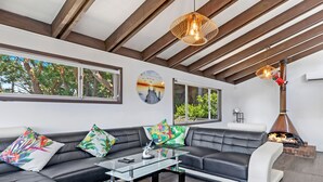 A modern living room with a sectional sofa, a glass coffee table, and a fireplace. - Kozyguru | Waterfront Holiday House With Kayak (Padstow Heights)