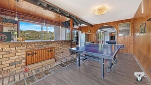 A room with a ping pong table, wooden walls, and a brick fireplace. - Kozyguru | Waterfront Holiday House With Kayak (Padstow Heights)