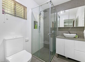 A modern bathroom with a glass-enclosed shower, a white toilet, and a vanity with a sink and mirror. - Kozyguru | Waterfront Holiday House With Kayak (Padstow Heights)