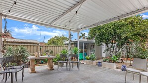 An outdoor patio area with a covered roof, a table, chairs, and various potted plants. - Kozyguru | Rockdale | Spacious 2 Bedrooms House (Rockdale)
