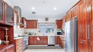 A kitchen with wooden cabinets, stainless steel appliances, and a window with plants. - Kozyguru | Rockdale | Spacious 2 Bedrooms House (Rockdale)
