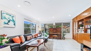A spacious living room with a piano, a sofa set, and a television. - Kozyguru | Rockdale | Spacious 2 Bedrooms House (Rockdale)