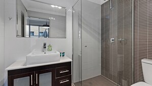A modern bathroom with a glass-enclosed shower, a white sink with toiletries, and a dark wooden vanity.