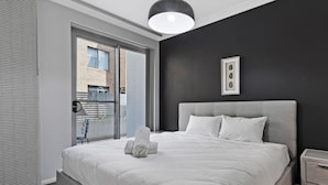 A modern bedroom with a large bed, a bedside table, a hanging light fixture, and a view of the outside through a sliding door.