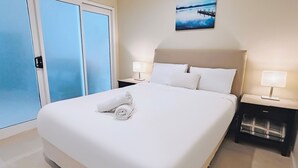 A hotel room with a bed, two bedside tables with lamps, a painting on the wall, and a view through the glass doors. - Kozyguru | Summer Hill | 1 Bed Townhouse (Summer Hill)