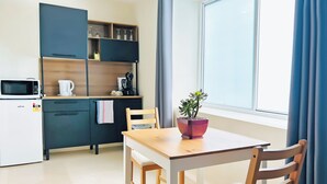 A compact kitchen with a microwave, kettle, and cabinets, a wooden dining table with chairs, and a window with curtains. - Kozyguru | Summer Hill | 1 Bed Townhouse (Summer Hill)