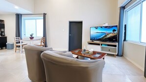 A modern living room with a flat-screen TV, two armchairs, a coffee table, and a dining area with a table and chairs. - Kozyguru | Summer Hill | 1 Bed Townhouse (Summer Hill)