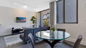 Ein modernes Wohnzimmer mit einem Glastisch, grauen Stühlen, einer Couch und einem Fernseher.