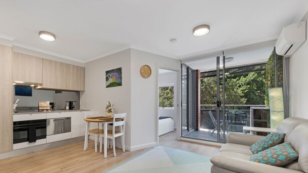 Eine moderne Wohnung mit Küche, Essbereich und einem Balkon mit Blick auf Bäume.