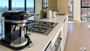 A modern kitchen with a gas stove, coffee maker, and a view of the city. - Kozyguru |St Leonards | 1 Bed Best Location & View (St Leonards)