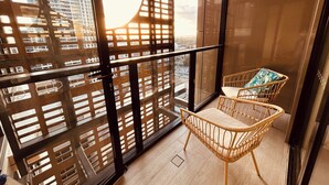 A balcony with a wicker chair and a view of a cityscape through a wooden lattice. - Kozyguru |St Leonards | 1 Bed Best Location & View (St Leonards)