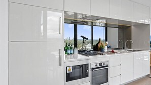 A modern kitchen with stainless steel appliances, a large window with a city view, and a telescope on the counter. - Kozyguru |St Leonards | 1 Bed Best Location & View (St Leonards)