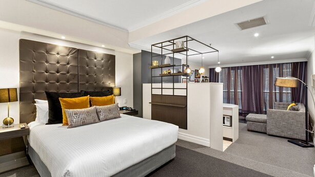 Quarto de hotel moderno com uma cama grande, uma escrivaninha, um sofá e TV integrada.