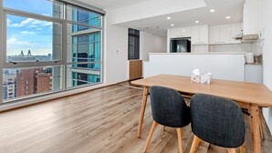 A modern kitchen with white cabinets, a black refrigerator, and a dining area with a wooden table and two chairs. - Kozyguru | Sydneycbd | Amazing City View 3B Apt (Sydney)