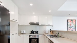 A modern kitchen with white cabinets, a stainless steel refrigerator, a built-in oven, a gas stove, and a sink. - Kozyguru | Sydneycbd | Amazing City View 3B Apt (Sydney)