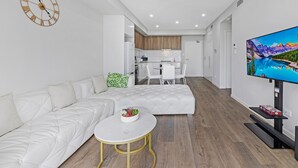 Una sala de estar moderna con un sofá blanco, una mesa de centro redonda y un televisor sobre un mueble.