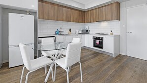Una cocina moderna con armarios blancos, una mesa de comedor de vidrio y sillas blancas.