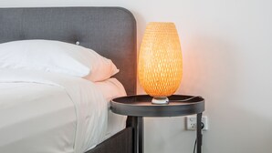 Una cama con ropa de cama blanca y una lámpara con textura sobre una mesita de noche.