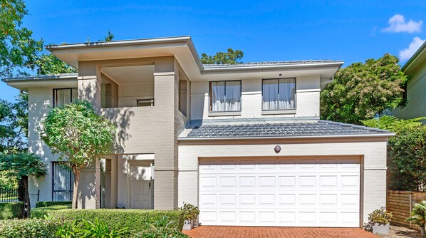 A two-story house with a white garage door, a balcony, and a small garden area. - Kozyguru | Westleigh | 4 Bed Room | Free Parking (Westleigh)