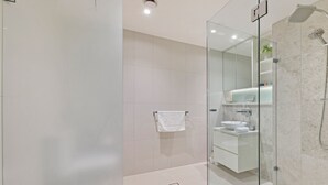 A modern bathroom with a glass shower enclosure, a white sink, and a glass door.