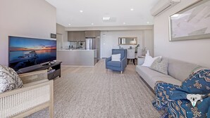 A modern living room with a flat-screen TV, a sofa, a blue armchair, and a patterned throw blanket. - Kozyguru | Wentworth Point | 2B Apt+Free Parking (Wentworth Point)