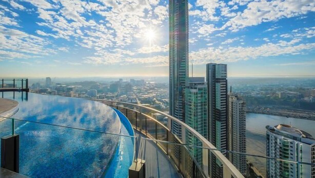Un edificio de gran altura con fachada de vidrio y un balcón curvo de cristal que ofrece vistas a la ciudad y al río.