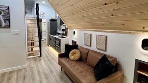 A modern living room with a brown leather sofa, wooden ceiling, and a kitchen in the background. - Cedar Nook (Wellsboro)