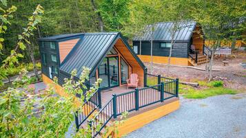 A cabin with a deck, a glass door entrance, and a small porch with chairs.