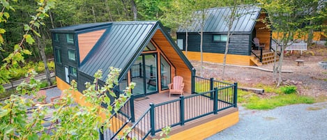 Una cabaña con terraza, puerta de cristal y un pequeño porche con sillas.