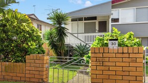 A residential property with a gated entrance, a brick wall with a mailbox, and a house with a grey exterior and a white fence. - Kozyguru | Mt Gravatt East | 3 Bed Home (Mount Gravatt East)