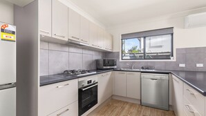A modern kitchen with white cabinets, a stainless steel dishwasher, a microwave, and a gas stove. - Kozyguru | Mt Gravatt East | 3 Bed Home (Mount Gravatt East)