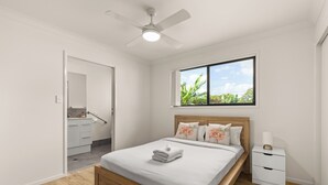 A bedroom with a wooden bed, white bedding, a nightstand, and a window with a view of greenery. - Kozyguru | Mt Gravatt East | 3 Bed Home (Mount Gravatt East)